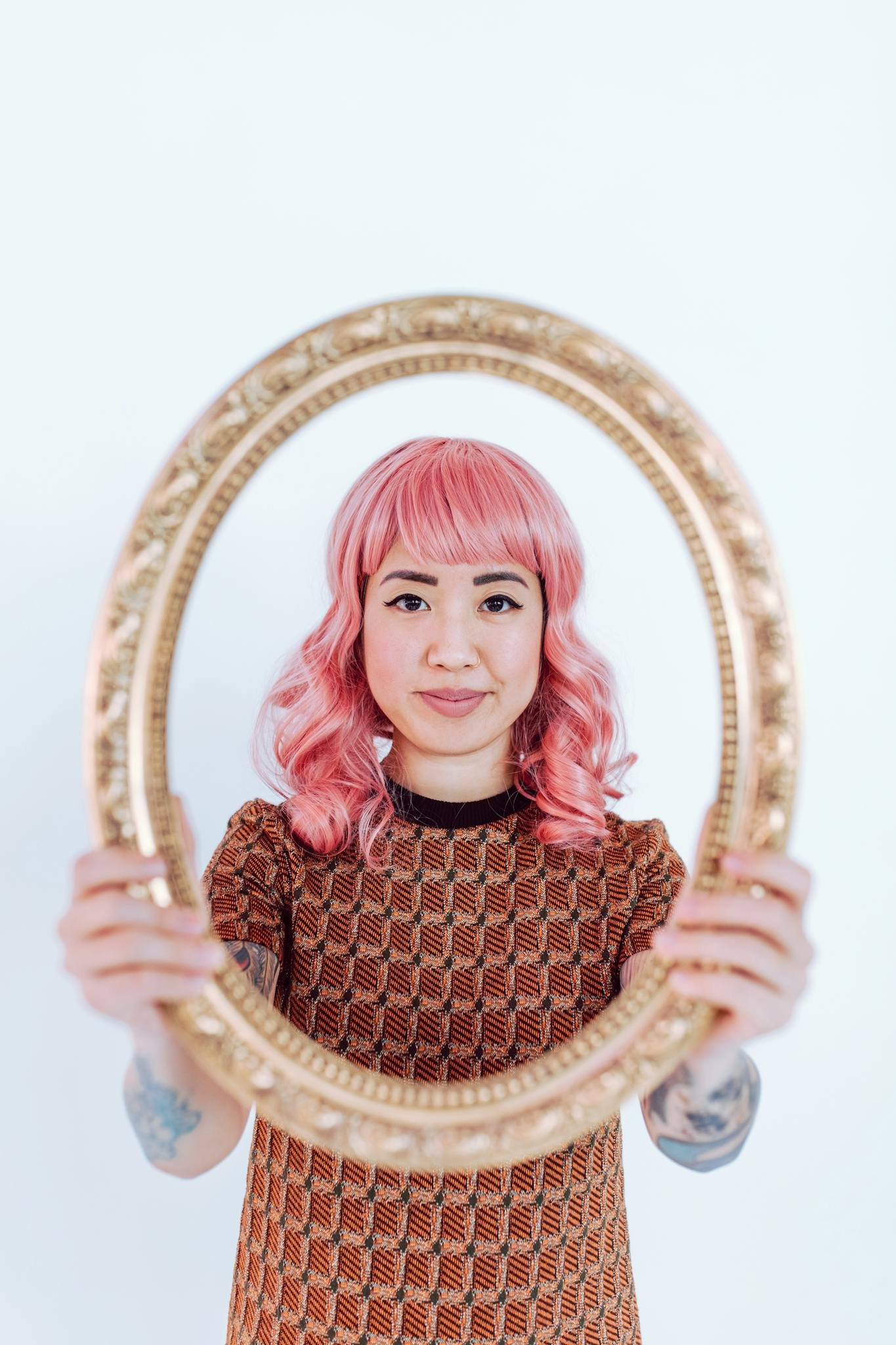 A woman with pink hair framed artfully in a vintage gold mirror, showcasing style.