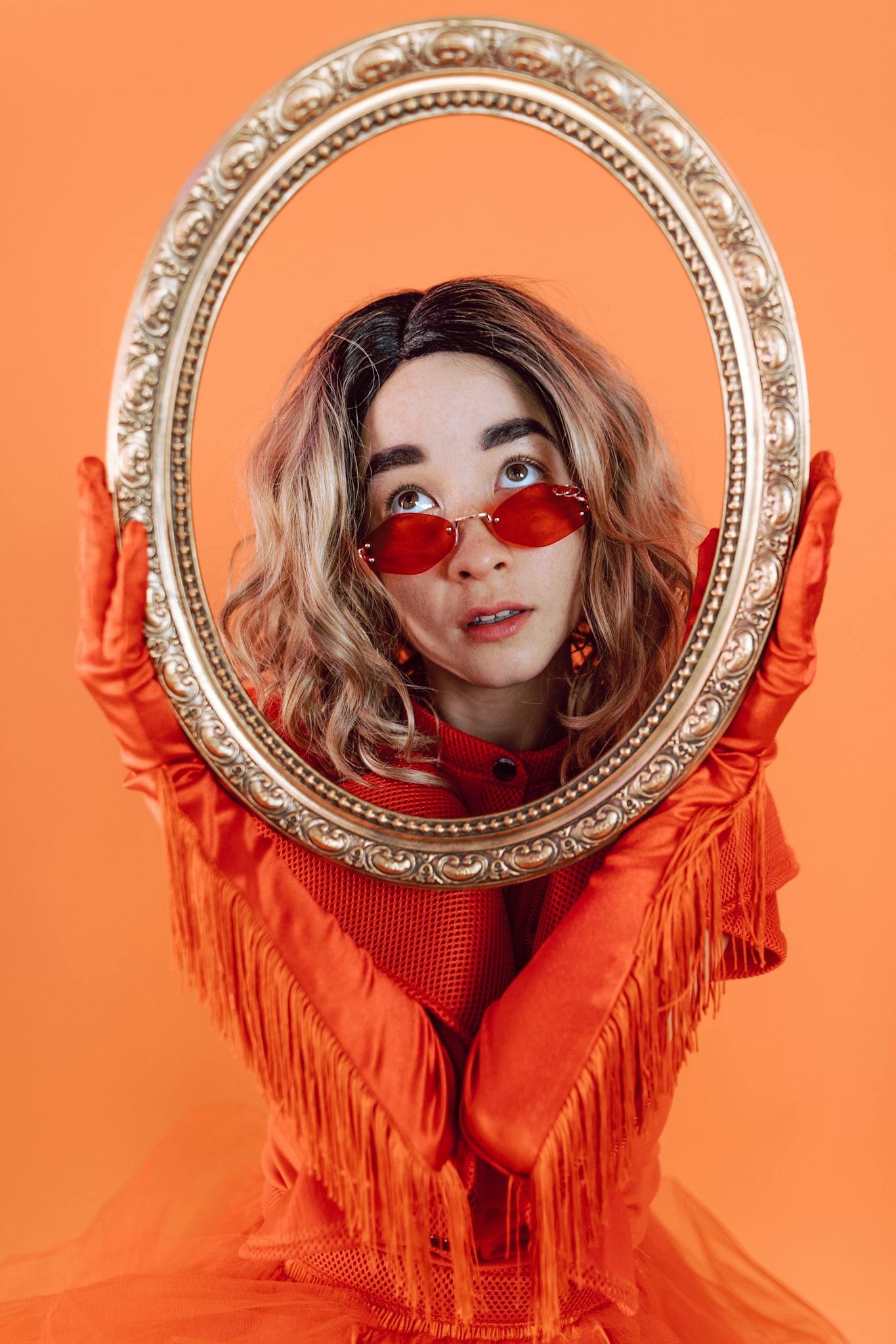 Fashionable woman in orange attire holding an ornate frame with a vibrant background.