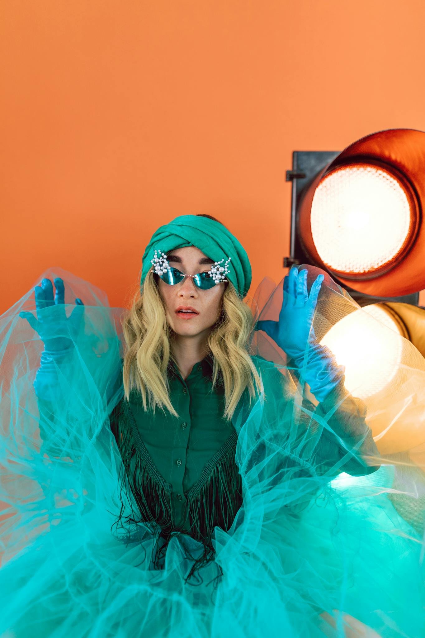 Stylish woman in vibrant outfit and sunglasses posing in studio with bright lighting.
